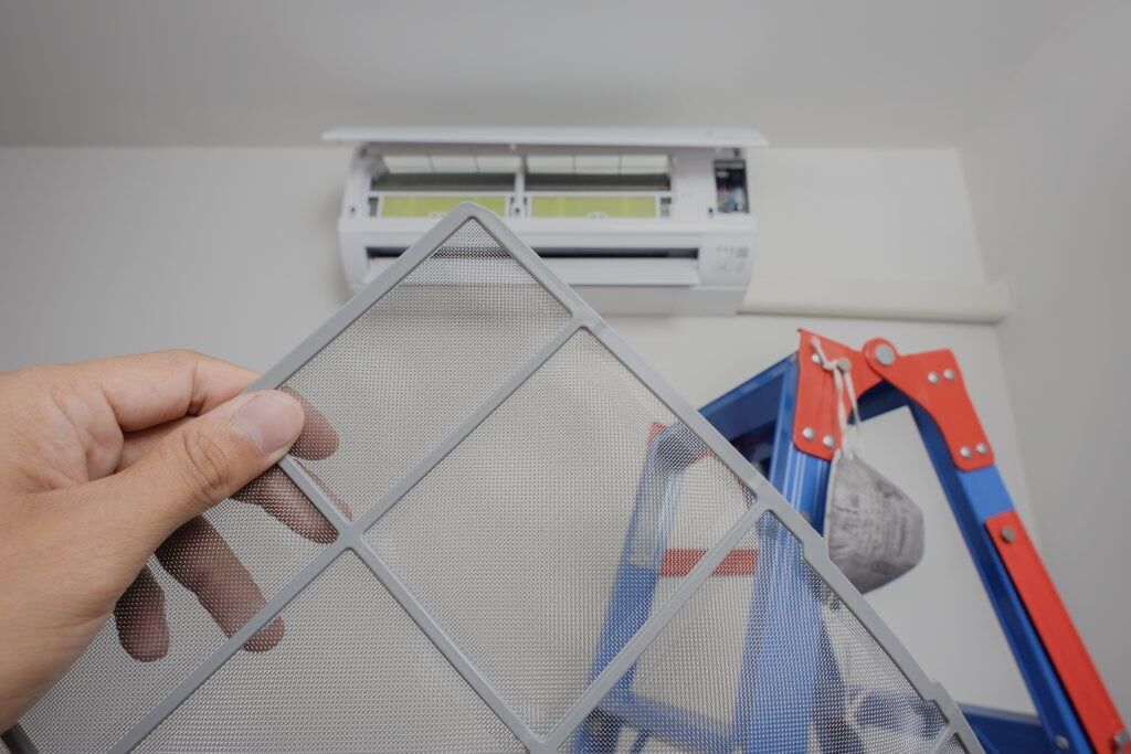 Wall mounted heat pump with hood open. Infront a technision is holding a filter and standing by a ladder