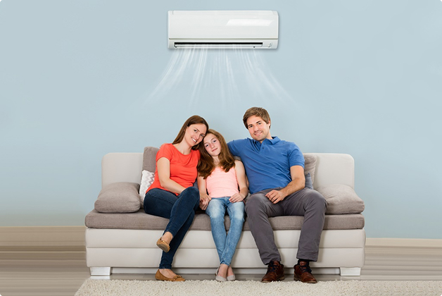 A happy family sitting on a couch, enjoying the cooling effects of a wall-mounted air conditioner.
