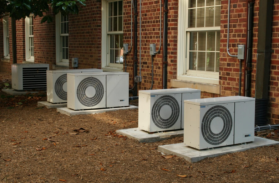 Outdoor units of HVAC systems on the exterior of a red-bricked residential home.